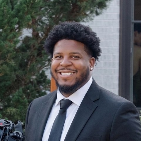Jasmil Moore in a black suit holding a cinema camera rig